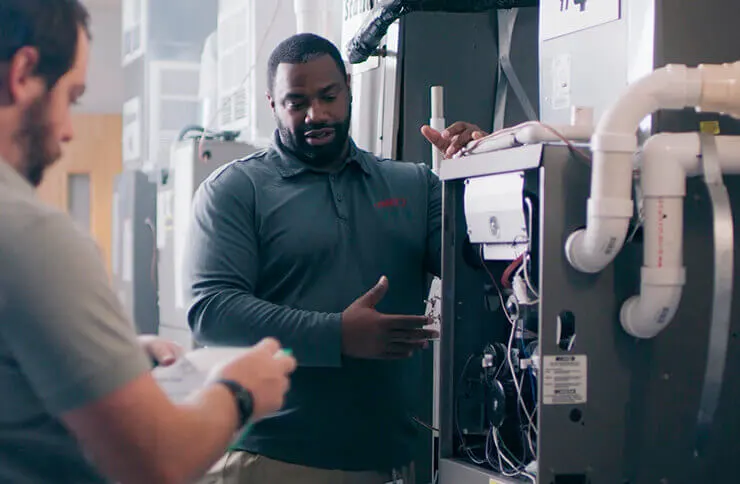 Two HVAC professionals work on a furnace installation in a building, ensuring optimal performance for The Chill Brothers.