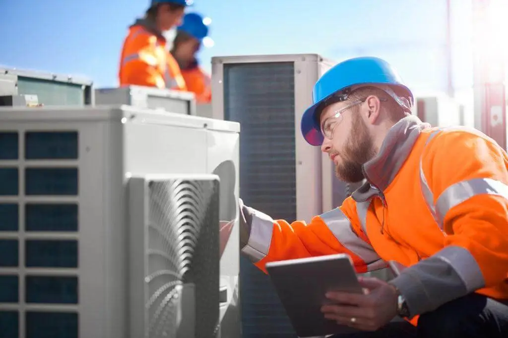 A man wearing an orange vest and hard hat assesses an air conditioner, showcasing furnace repair expertise in Houston.