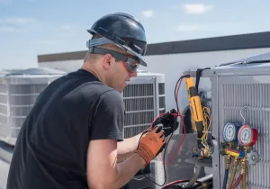 A man in a hard hat and safety glasses repairs an air conditioning unit, representing HVAC services in Austin, TX.