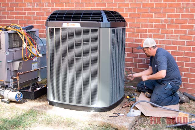 Technician servicing an outdoor Trane air conditioner next to a brick wall.